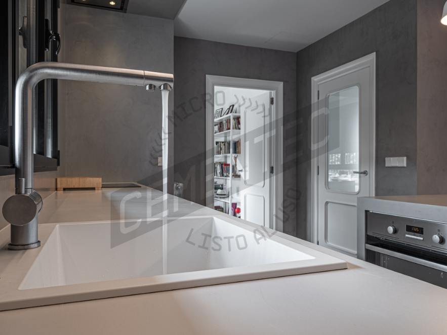 Kitchen reforms in microcement kitchens made by Cementec in which an island with an open tap can be seen.