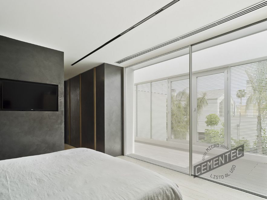 Microcemento en dormitorios aplicado por Cementec, en habitación con ventanal grande y suelo de parquet. 