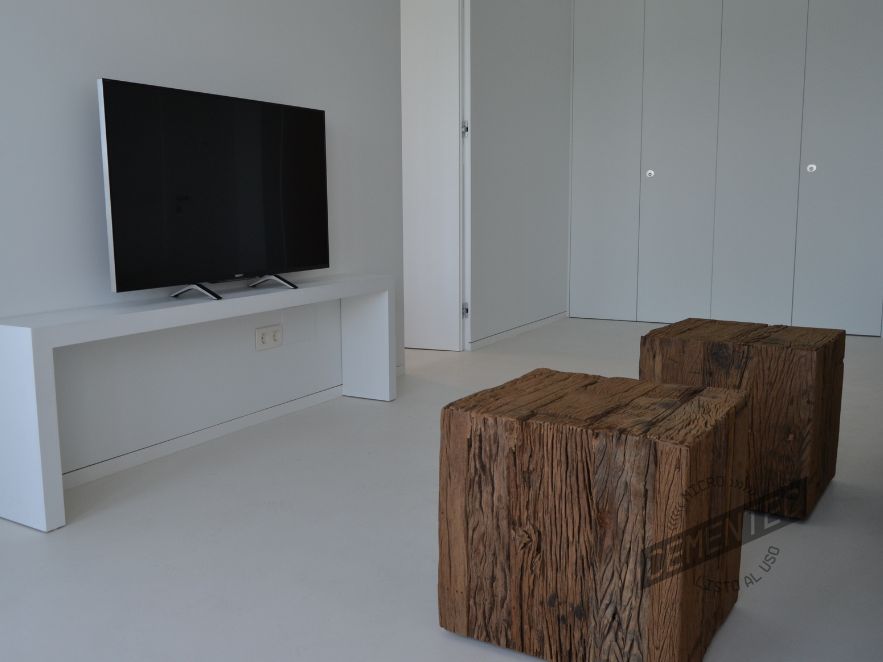 Salón con dos banquetas de madera y microcemento blanco aplicado sobre las paredes y suelo de una vivienda particular.