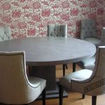 Microcement dining room table with chairs around it, wall with chromatic wallpaper pattern and parquet floor.