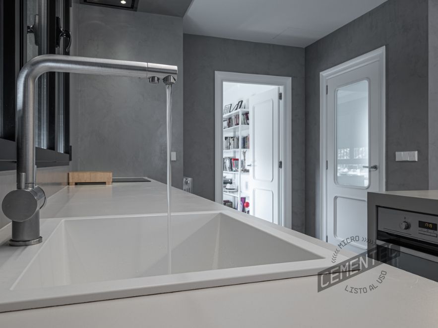 Close-up of a kitchen in white finish microcement on worktop, showing a sink with open tap.