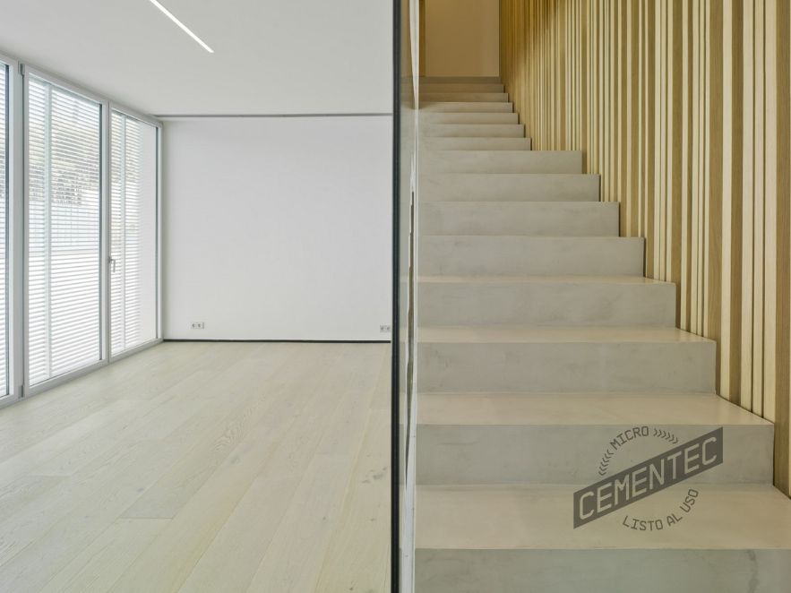 Imagen frontal de salón con escaleras de microcemento y madera en el suelo y en los acabados de la pared de la escalera.